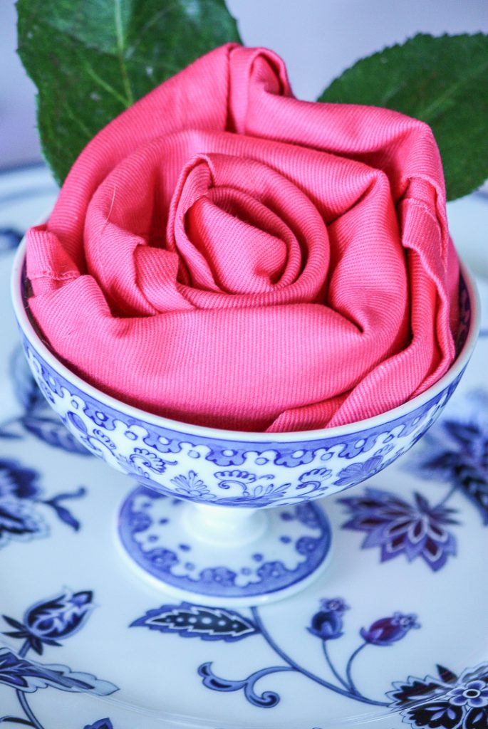 blue and white bowl with hot pink napkin tucked in it like a rose