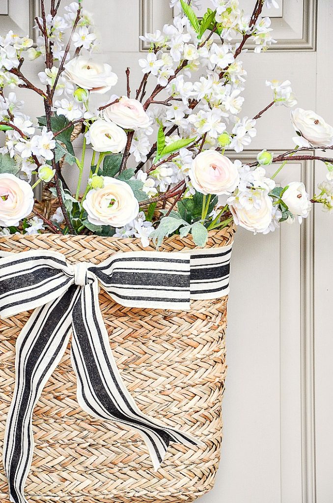 basket on the front door filled with apple blossom branches and ranunculus. Ties with a black and white ribbon