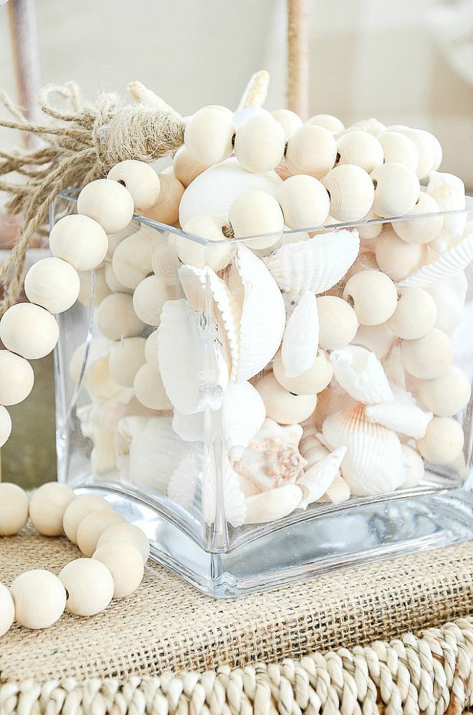 A CLEAR CUBE FILLED WITH SHELLS AND BEADS IN A SUMMER VIGNETTE