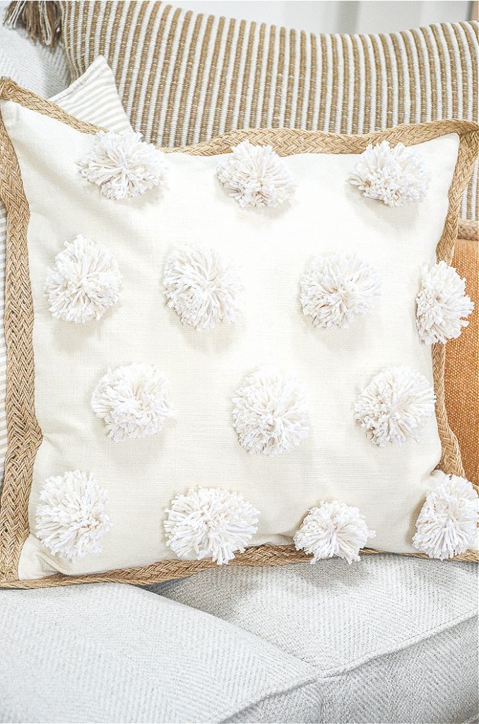 Trio of pillow on a sofa- featured pillow has pom-poms on the front of it