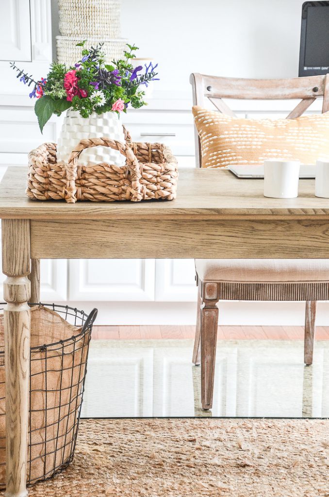 desk in a home office with a basket and a white vase of flowers on it