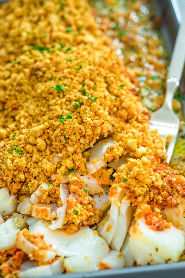 close up of a breadcrumb topped baked cod being stuck with a fork