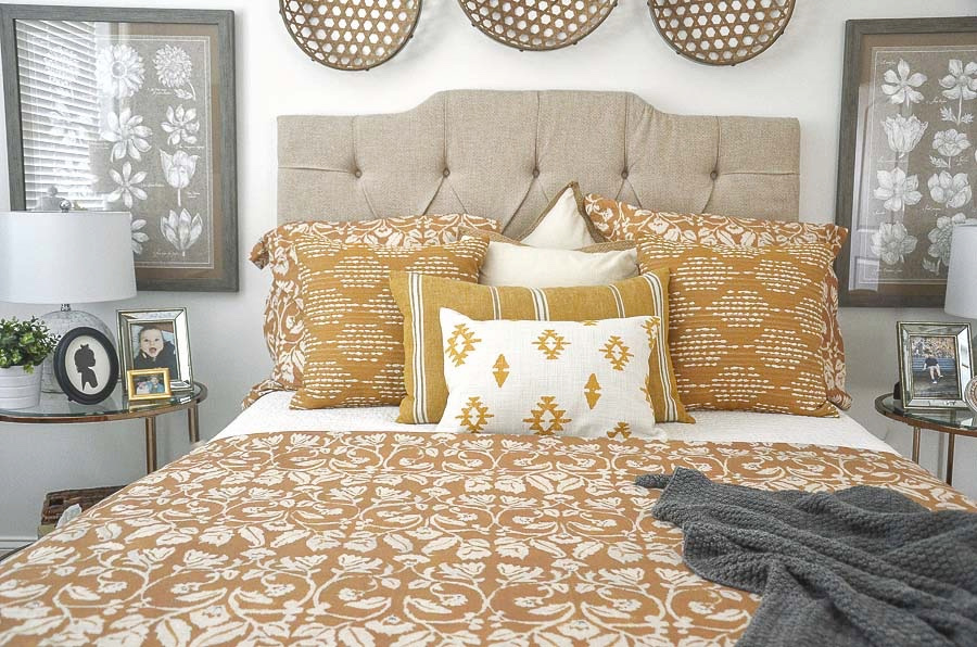 bed with neutral padded headboard and gold duvet and coordinating pillows with a gray throw