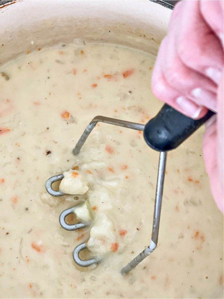 MASHING THE POTATOES IN THE SOUP WITH A POTATO MASHER