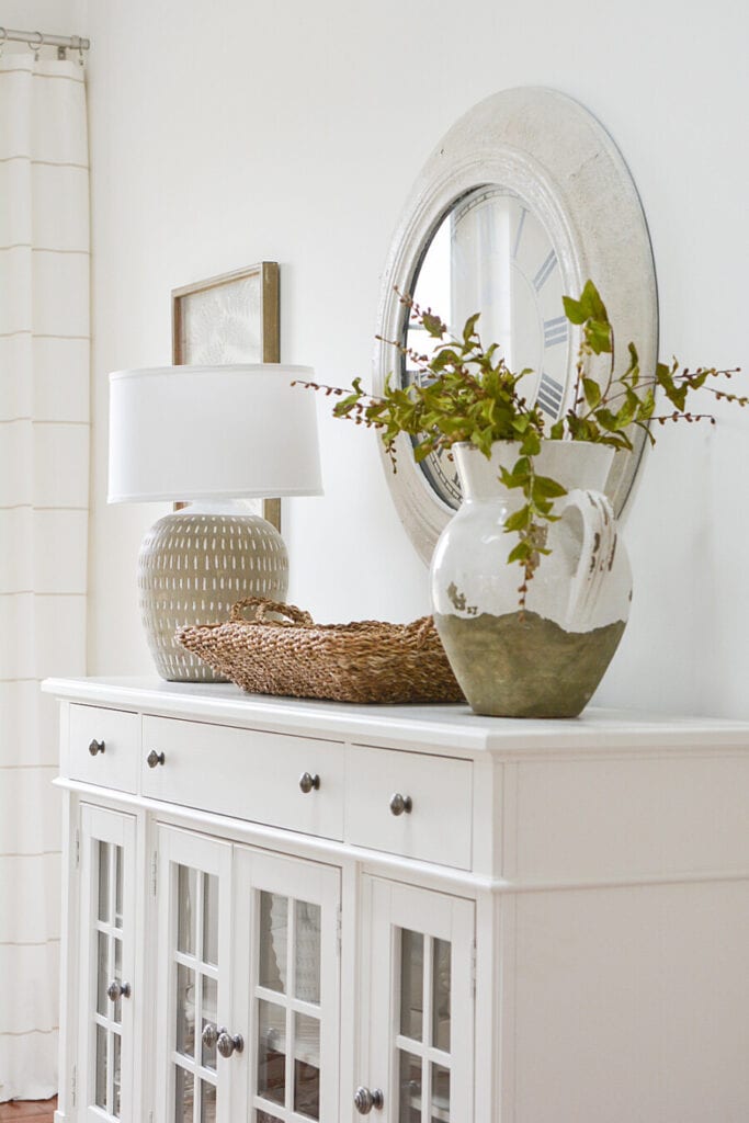 white buffet with lamp, baskets and an urn filled with greens for a post about stuck with decor