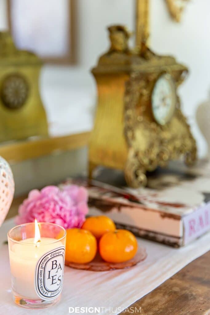 a dresser with a clock, bowl of oranges and a candle on it.