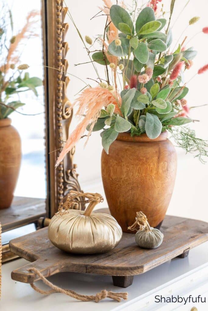 a vase, and two pumpkins on a wooden tray