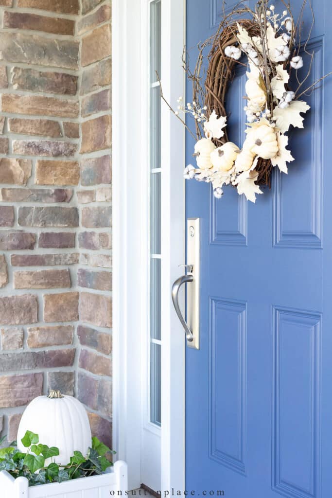 fall porch with blue front door and a neutral wreath on the front door