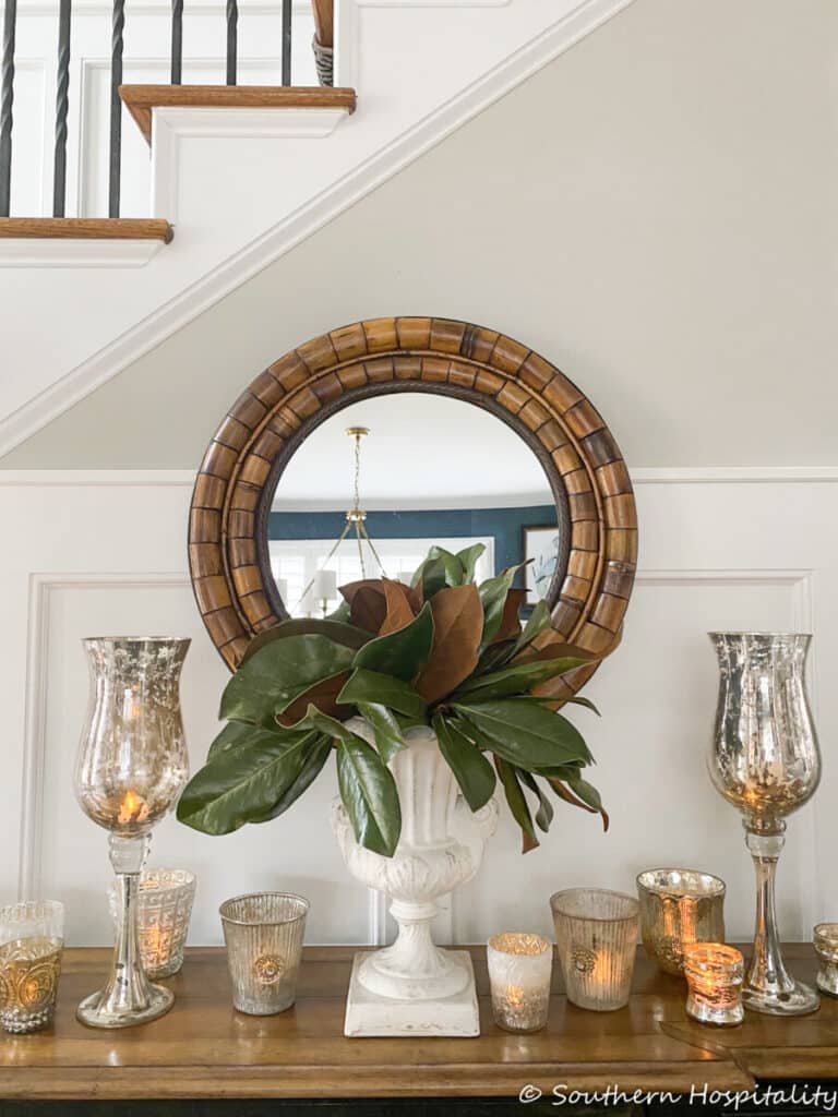 foyer with a round mirror, an urn of magnolias and candles