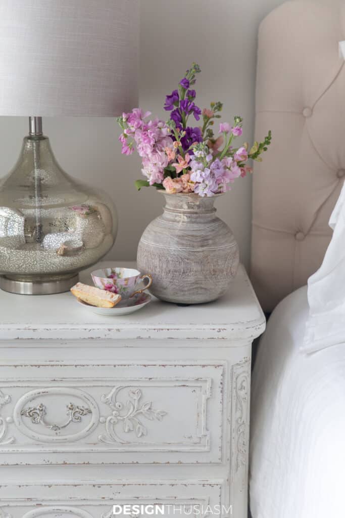 french bedside table with flowers and a pretty cup and saucer with biscotti