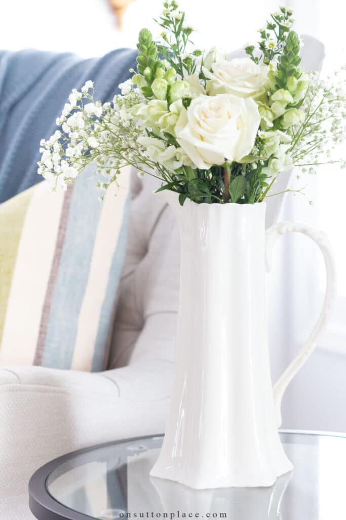 white pitcher with flowers on a glass end table.