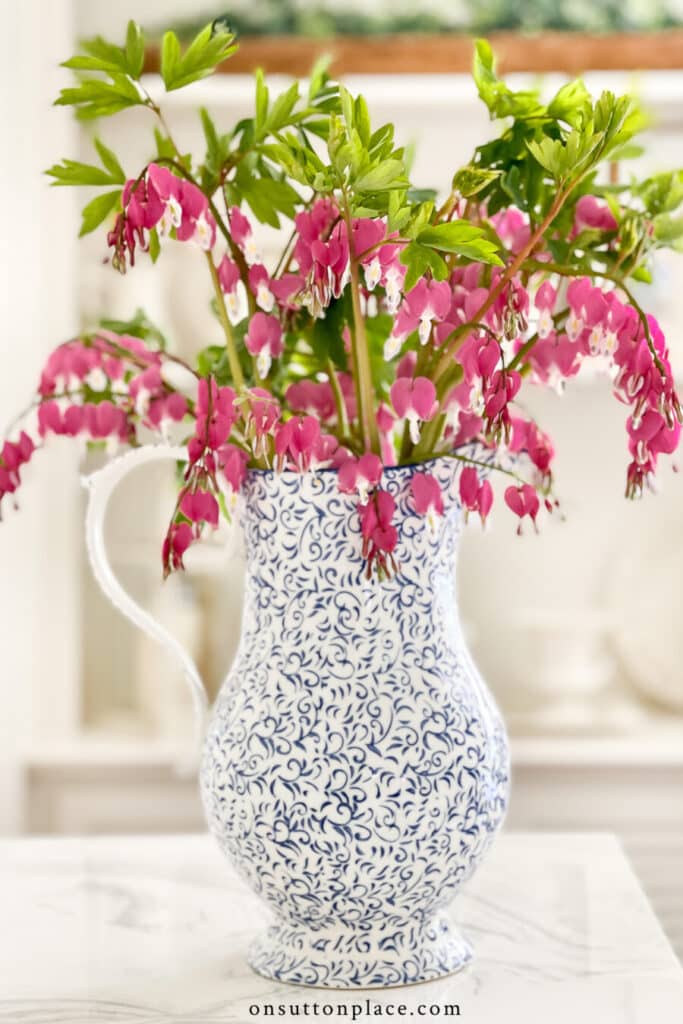 a blue and white pitcher with pink bleeding hearts