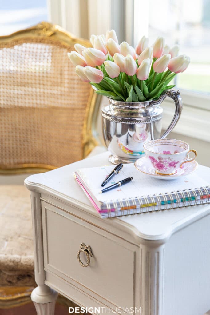 notebook with pens on a table and a silver urn with tulips