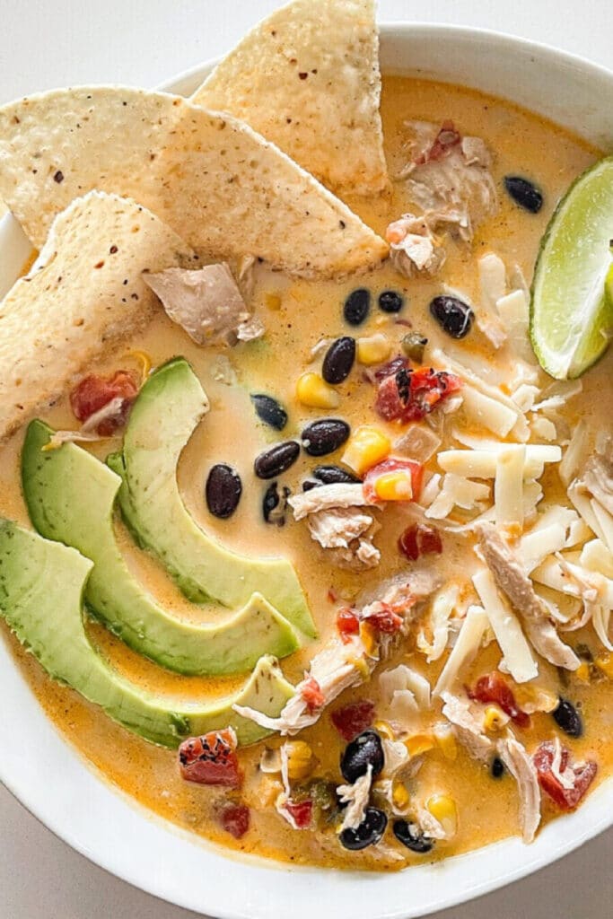 White Chicken Chili in a bowl with tortilla chips, avocado and limes