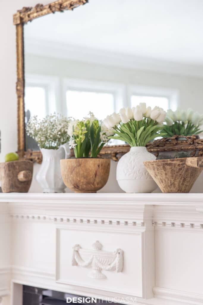 mantel with wooden bowls and white vases of spring flowers