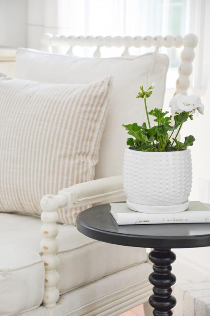 HOME LOVE-A SMALL TABLE NEXT TO A WHITE CHAIR WITH A POTTED GERANIUM