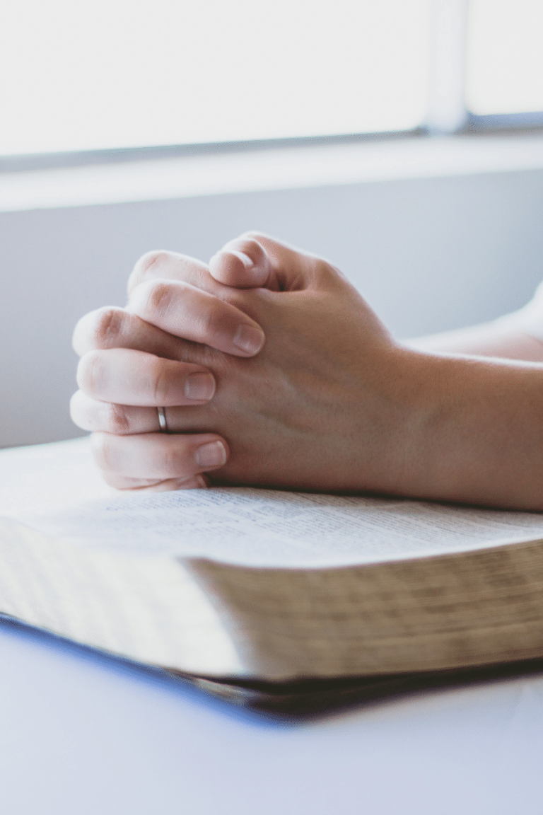 folded hands in prayer on top of a Bible