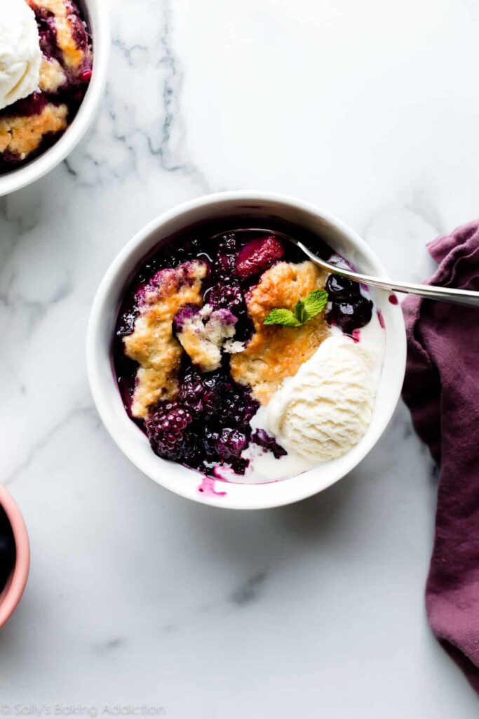 berry cobbler in a bowl with vanilla ice cream.
